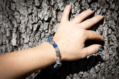 Hand wearing a beaded cremation bracelet against a tree bark background